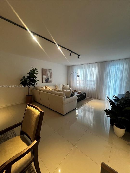 Large-format polished floor tile, adjustable black track lighting, and wall-to-wall floor-to-ceiling drapery