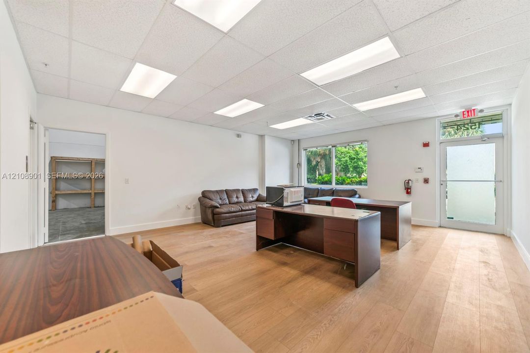 Open-concept interior space featuring wood-finish flooring, recessed acoustic tile ceiling with integrated lighting, and a glass-paneled entry door