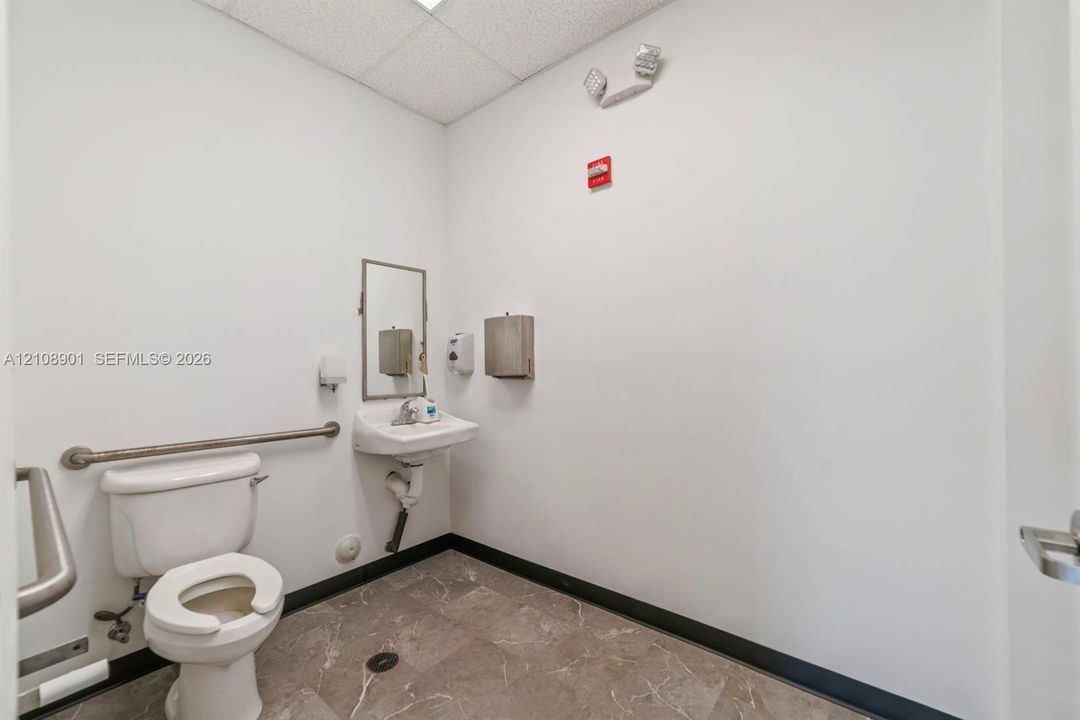 Restroom featuring stone-finish flooring, a wall-mounted sink, and metal grab bars