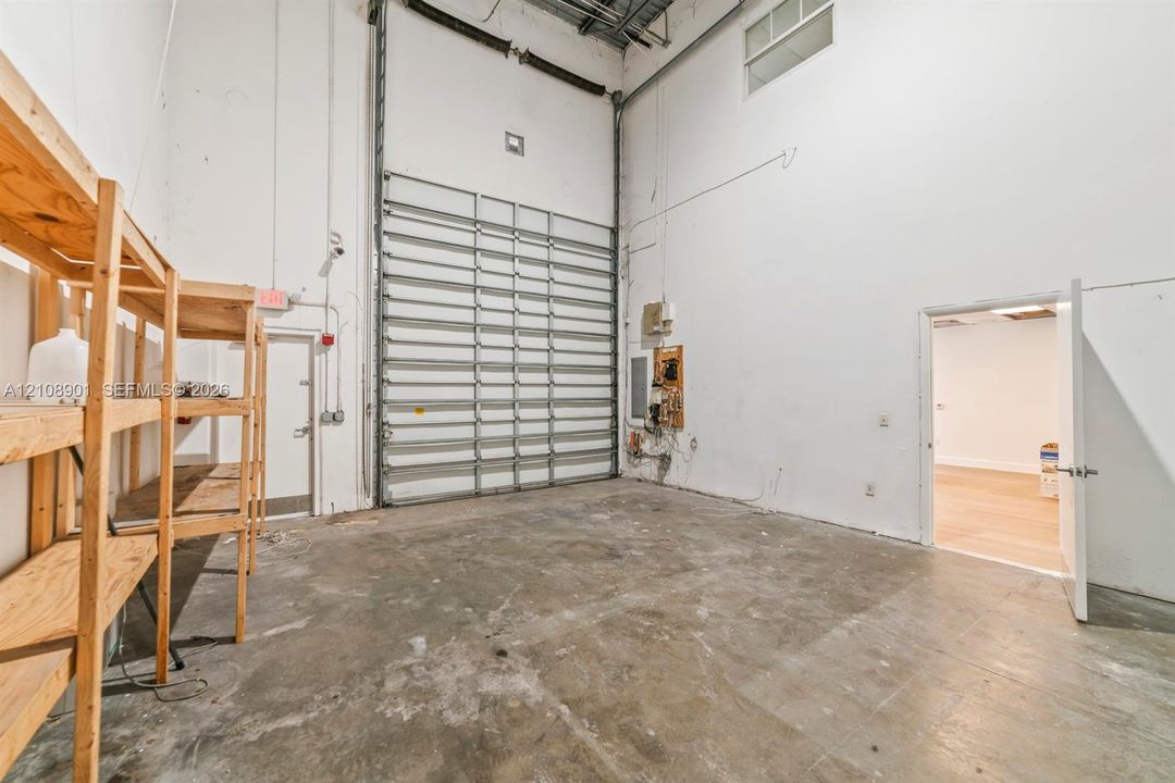 Industrial workspace featuring high ceilings, a large roll-up metal door, and concrete flooring