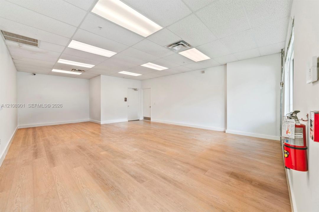 Open-concept interior featuring light wood-finish flooring, white walls, and a drop ceiling with recessed rectangular lighting