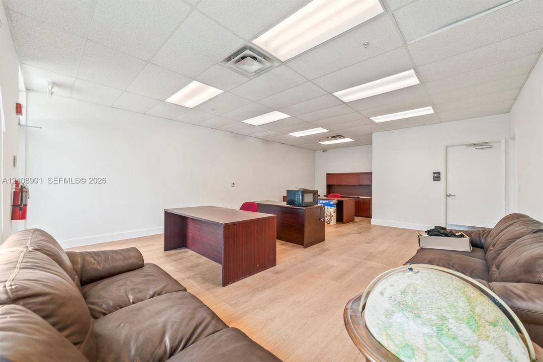 Open-concept interior featuring wood-finish flooring, recessed drop-ceiling grid, and integrated fluorescent lighting fixtures