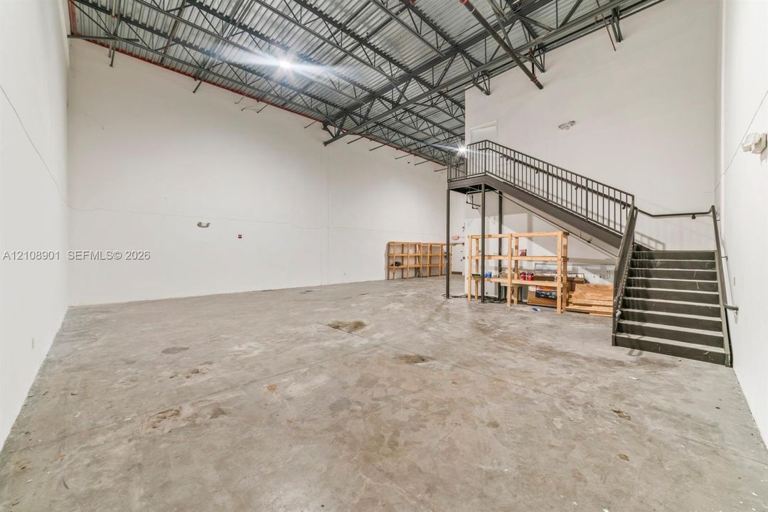 Industrial space featuring high-clearance exposed steel truss ceiling, concrete flooring, and metal staircase with handrails