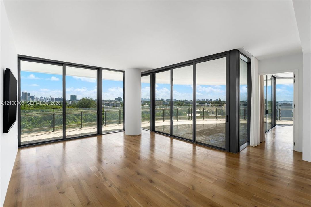 Floor-to-ceiling glass sliding doors, wood-finish flooring, and a wrap-around balcony with industrial-style metal railing