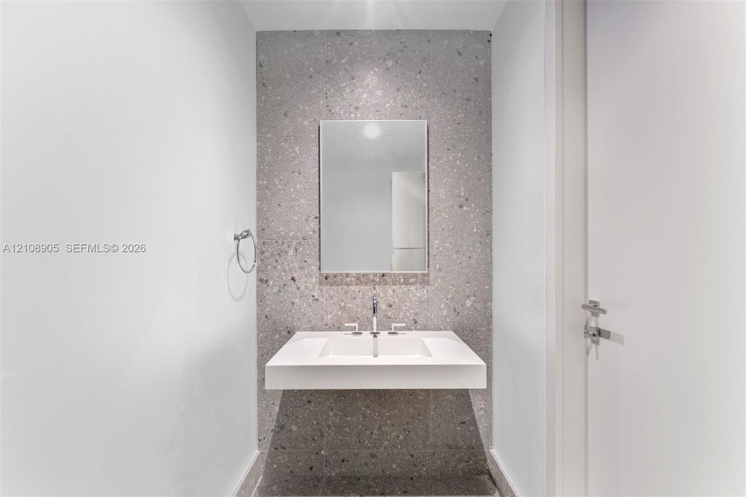 Floating vanity featuring an integrated rectangular sink, wall-mounted faucet, full-height terrazzo tile accent wall, and a framed mirror
