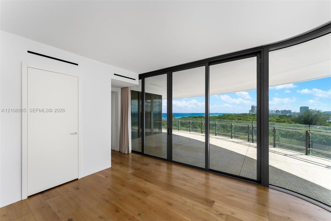 Floor-to-ceiling sliding glass doors, wood-finish flooring, and expansive covered balcony with glass railing