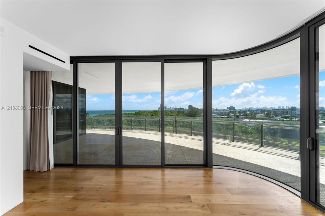 Curved floor-to-ceiling glass walls, expansive wraparound terrace, dark-framed sliding glass doors, and wide-plank wood-finish flooring
