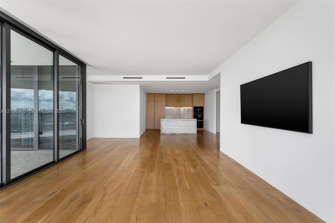 Open-concept interior featuring wood-finish flooring, floor-to-ceiling sliding glass doors, recessed ceiling lighting, and a kitchen with custom wood-finish cabinetry and a stone-clad central island