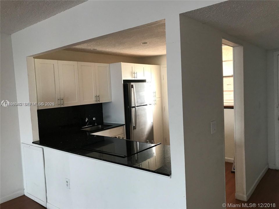Kitchen featuring white shaker-style cabinetry, dark stone countertops, an integrated cooktop, and stainless steel refrigerator