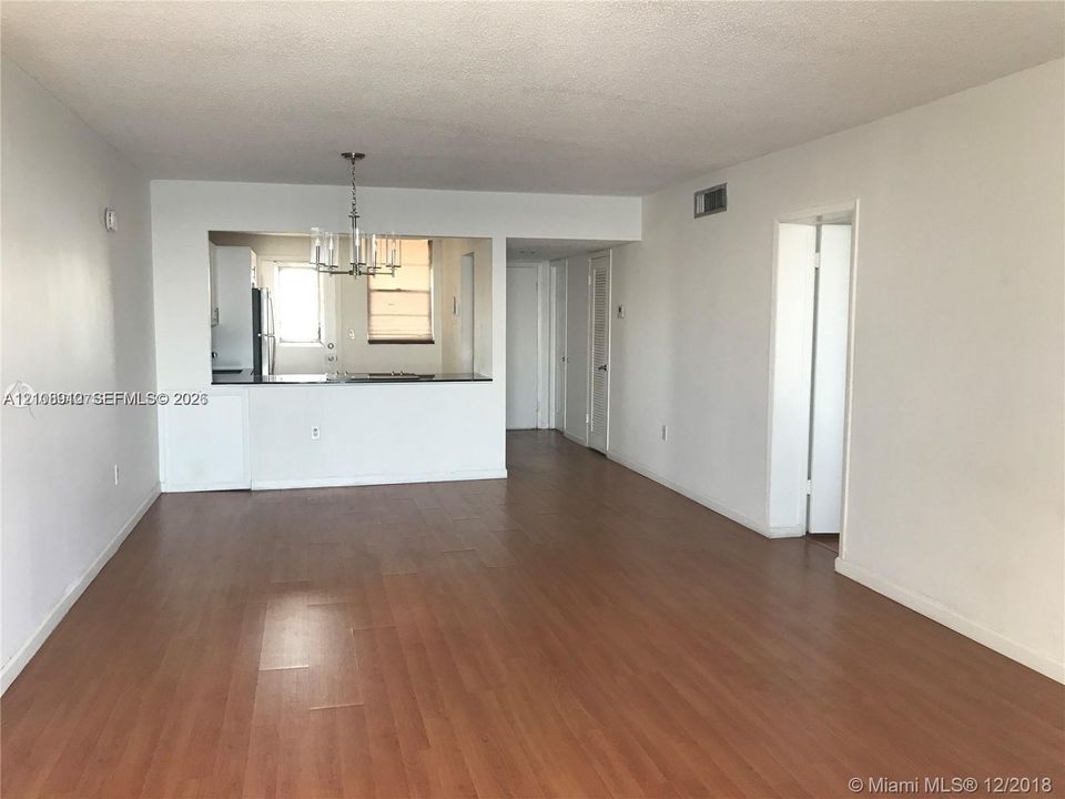 Open-concept interior featuring wood-finish flooring, a pass-through kitchen window, and a multi-arm metal chandelier