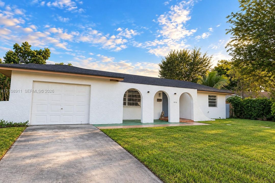 Stucco exterior featuring arched architectural detailing, a covered porch, an attached one-car garage, a concrete driveway, and a manicured front lawn