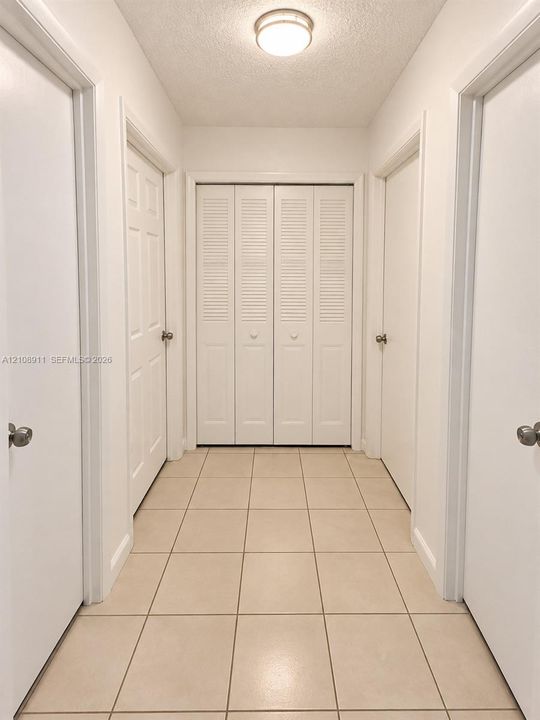Neutral-toned tile flooring, flush-mount ceiling lighting, and built-in closet with louvered bifold doors
