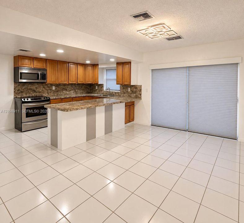 Kitchen featuring wood cabinetry, stone-finish countertops, stainless steel appliances, ceramic tile flooring, and sliding glass doors