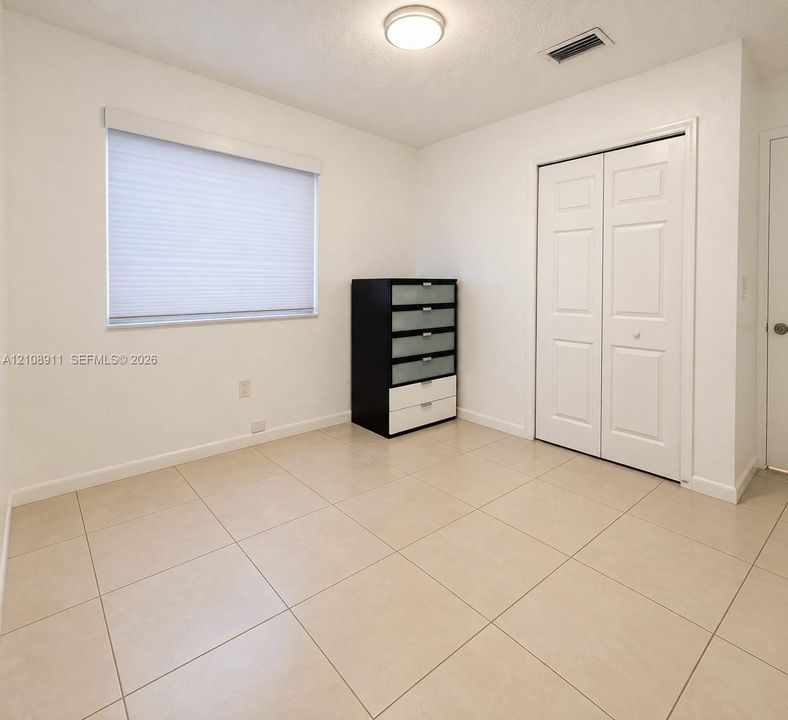 Neutral-toned tile flooring, white interior walls, pleated window shade, and double-panel closet doors