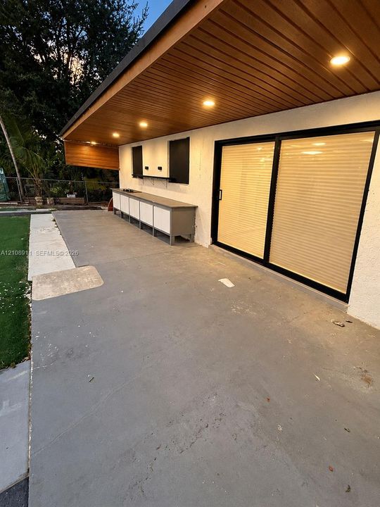 Covered concrete patio featuring a wood-paneled ceiling with recessed lighting, built-in cabinetry, and black-framed sliding glass doors