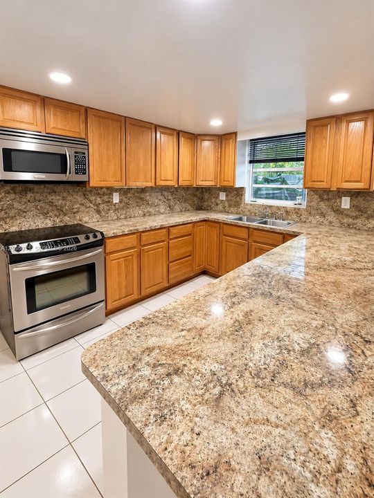 Kitchen featuring wood cabinetry, stone-finish countertops, stainless steel appliances, a double-basin sink, and tile flooring