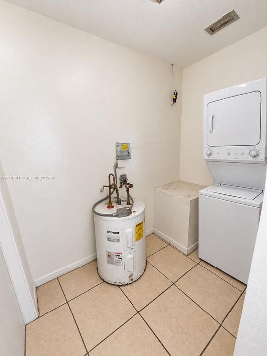 Utility area featuring ceramic tile flooring, a vertical stacked laundry unit, and an electric water heater
