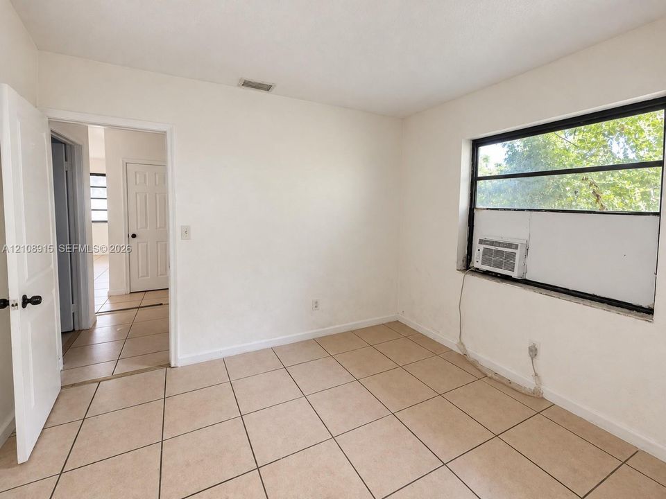 Interior space featuring neutral tile flooring, smooth wall finishes, a multi-pane window with dark framing, and a white interior door