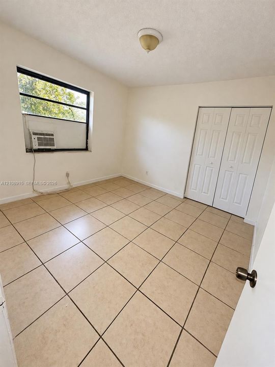 Neutral-toned tile flooring, light-colored walls, window with black framing, and white bi-fold closet doors