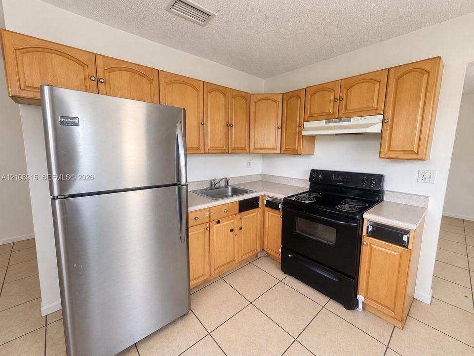 Kitchen featuring wooden cabinetry, laminate countertops, stainless steel refrigerator, black electric range, and tile flooring
