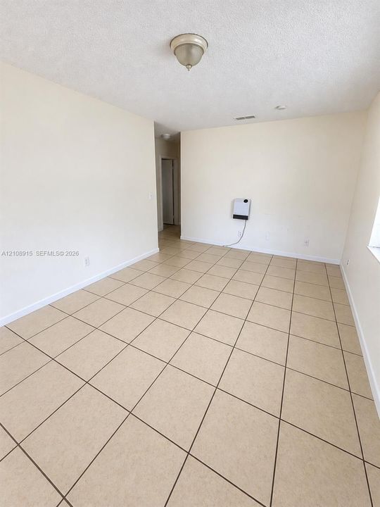Neutral interior space featuring large-format ceramic floor tiles, smooth-finish walls, and a center-mounted flush mount light fixture
