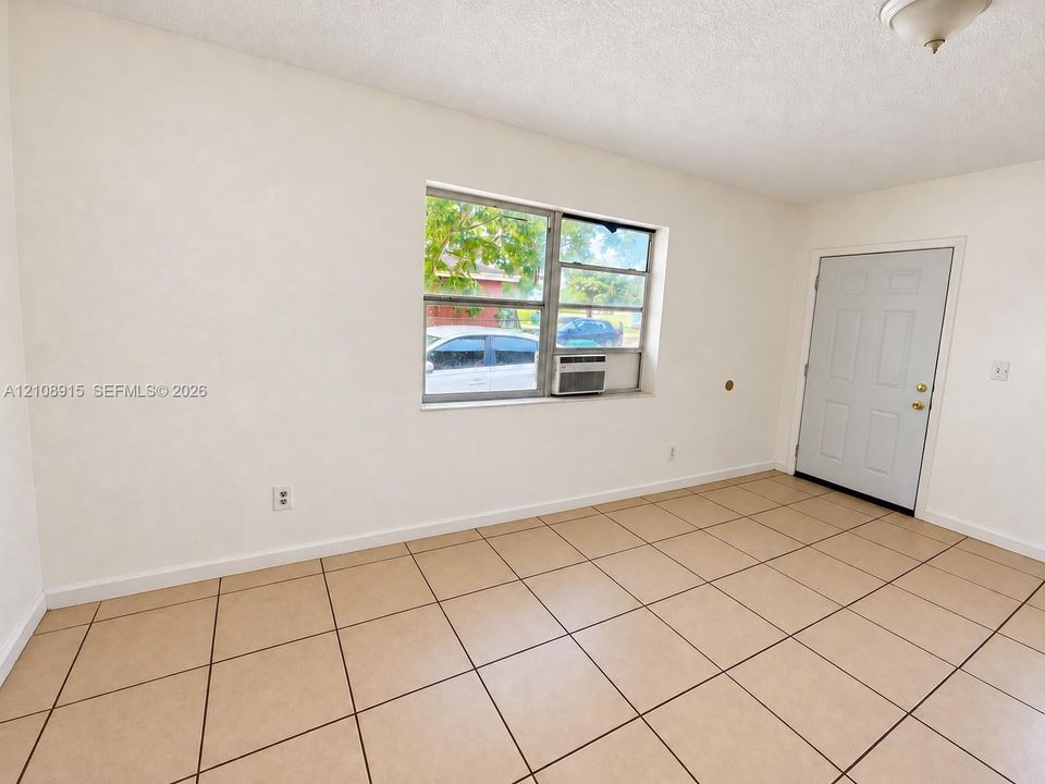 Neutral-toned tile flooring, solid-panel exterior door, sliding window, and ceiling-mounted light fixture