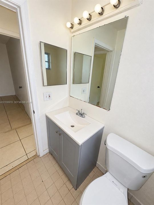Vanity featuring a gray cabinet base with a white countertop, an integrated rectangular sink with a chrome faucet, a wall-mounted vanity mirror, and a five-light fixture