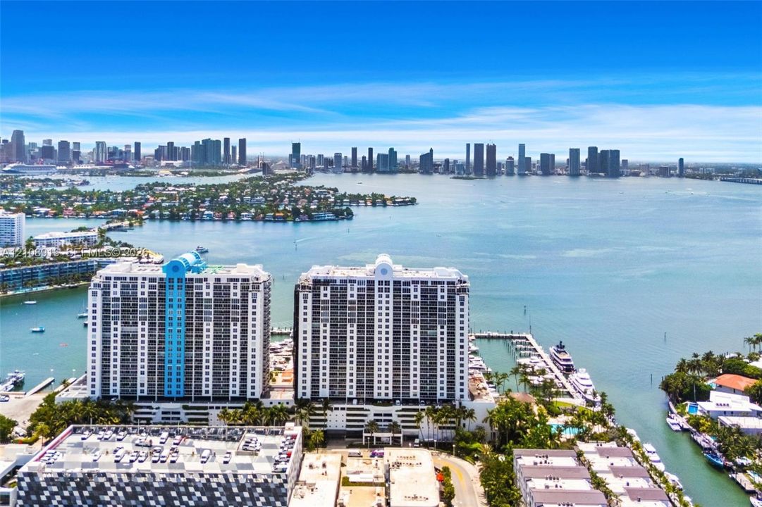 Aerial perspective of Sunset Harbour Building waterfront high-rise residential towers. Unit is located on the bayside of the North Tower (all white building).