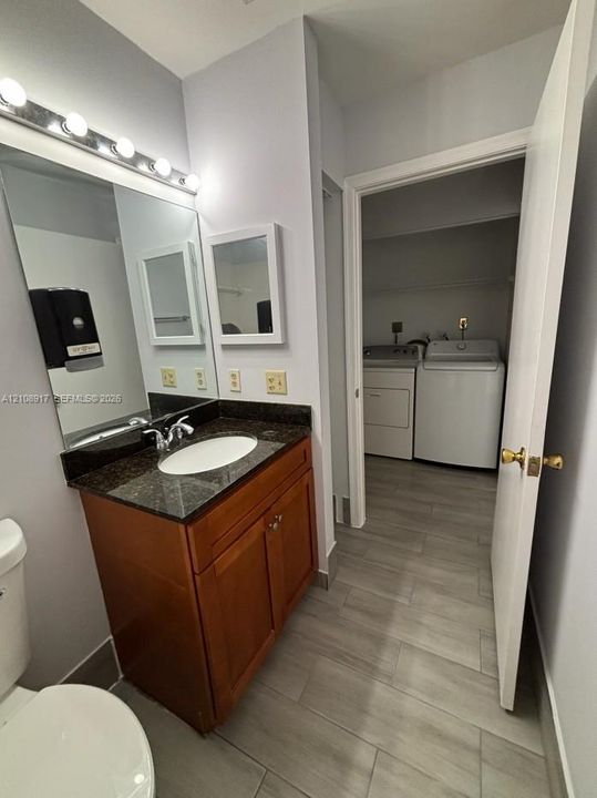Vanity featuring a dark stone-finish countertop, under-mount oval basin, and wood-finish cabinetry, complemented by a large wall-mounted mirror and multi-bulb vanity lighting