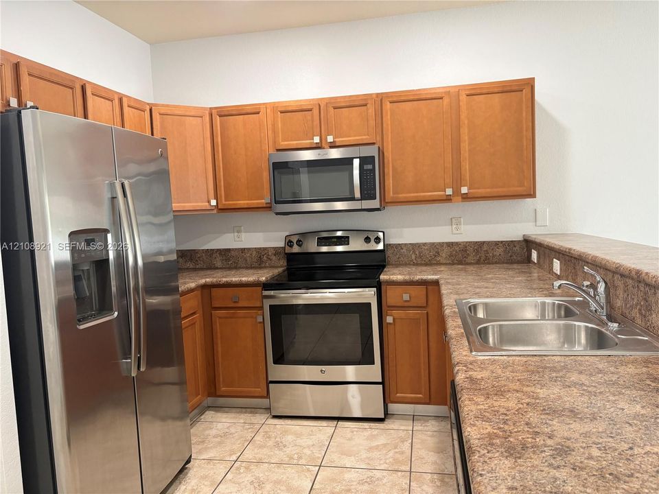 Kitchen featuring wooden cabinetry, solid surface countertops, stainless steel appliances, and tile flooring
