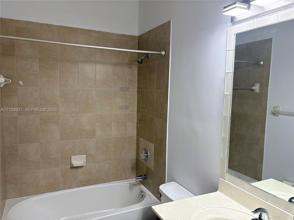 Bathroom featuring a tub and shower combination with neutral tile surround, vanity with an integrated basin, wall-mounted mirror with tiled border, and modern multi-bulb lighting fixture