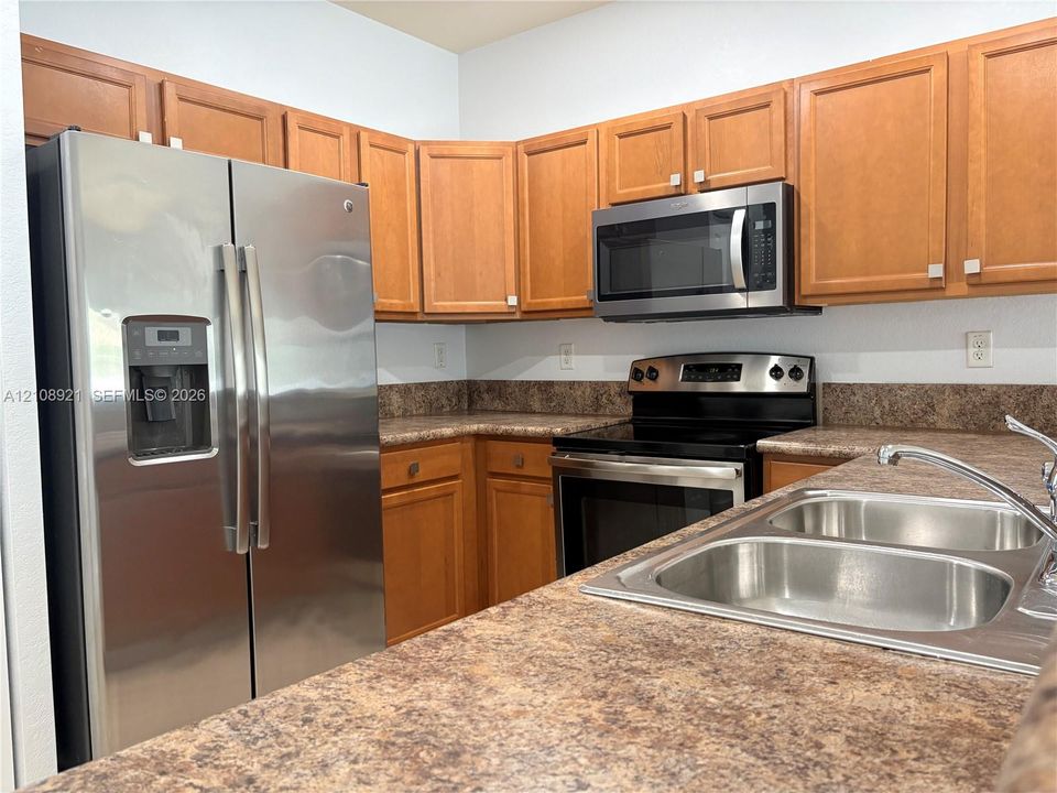 Kitchen featuring wood cabinetry, stainless steel side-by-side refrigerator, built-in microwave, range, and double-basin stainless steel sink with a laminate countertop