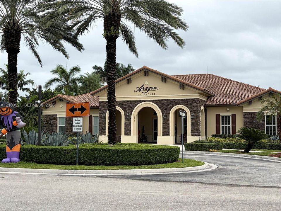 Community clubhouse featuring a stucco and stone veneer exterior, arched entryways, and a tiled roof, surrounded by manicured landscaping and mature palm trees