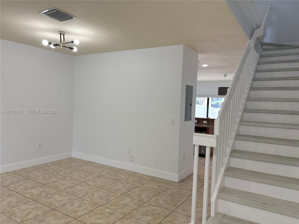 Staircase featuring white balusters and wood-finish treads, complemented by neutral tile flooring and a multi-bulb modern chandelier