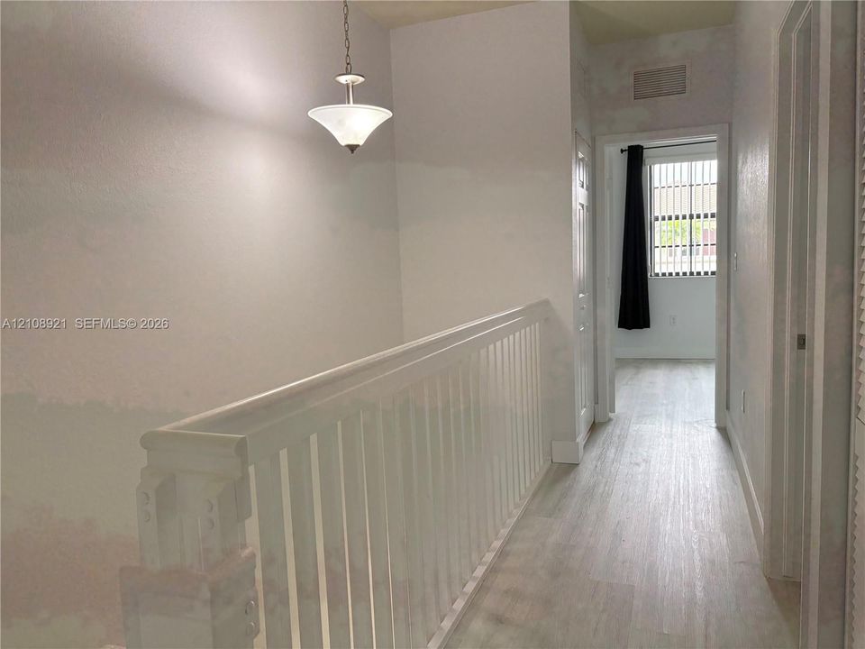 White wooden balustrade, wood-finish flooring, and a pendant light fixture