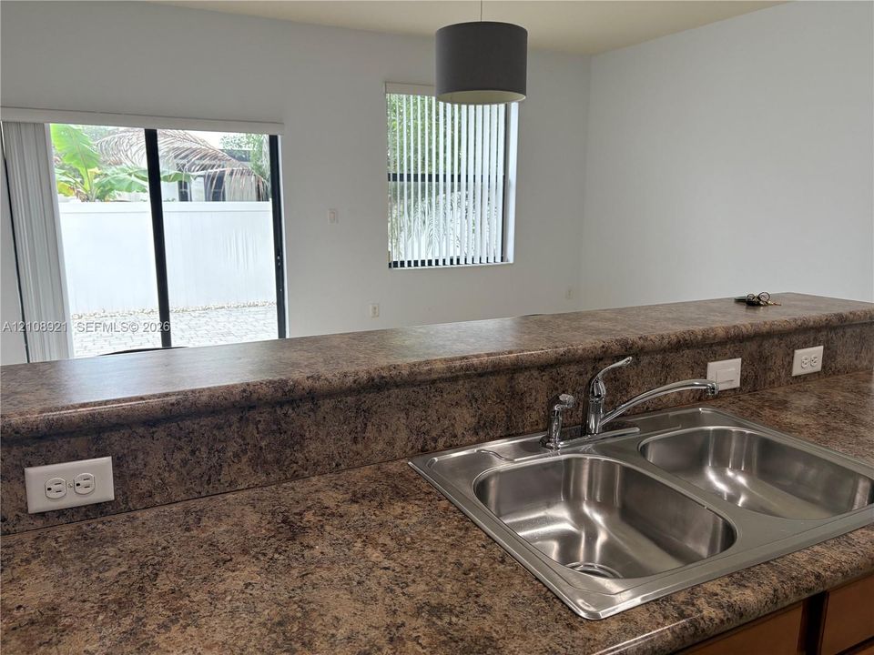 Kitchen featuring laminate countertops, a dual-basin stainless steel sink with a pull-out sprayer faucet, vertical window blinds, and a drum pendant light fixture