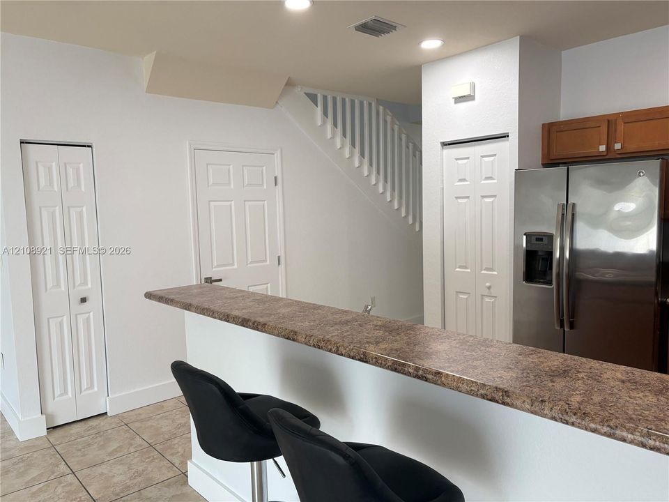 Kitchen featuring a breakfast bar with stone-finish countertop, stainless steel refrigerator, recessed lighting, and tile flooring