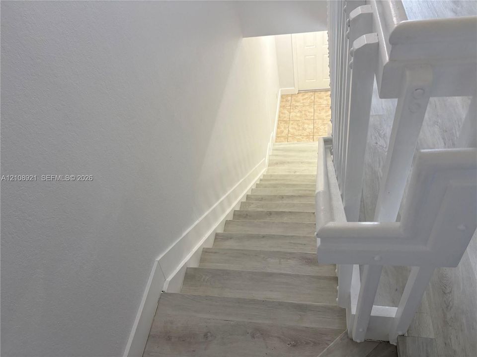 Staircase featuring wood-finish flooring, white painted millwork, and a matching painted handrail with vertical balusters