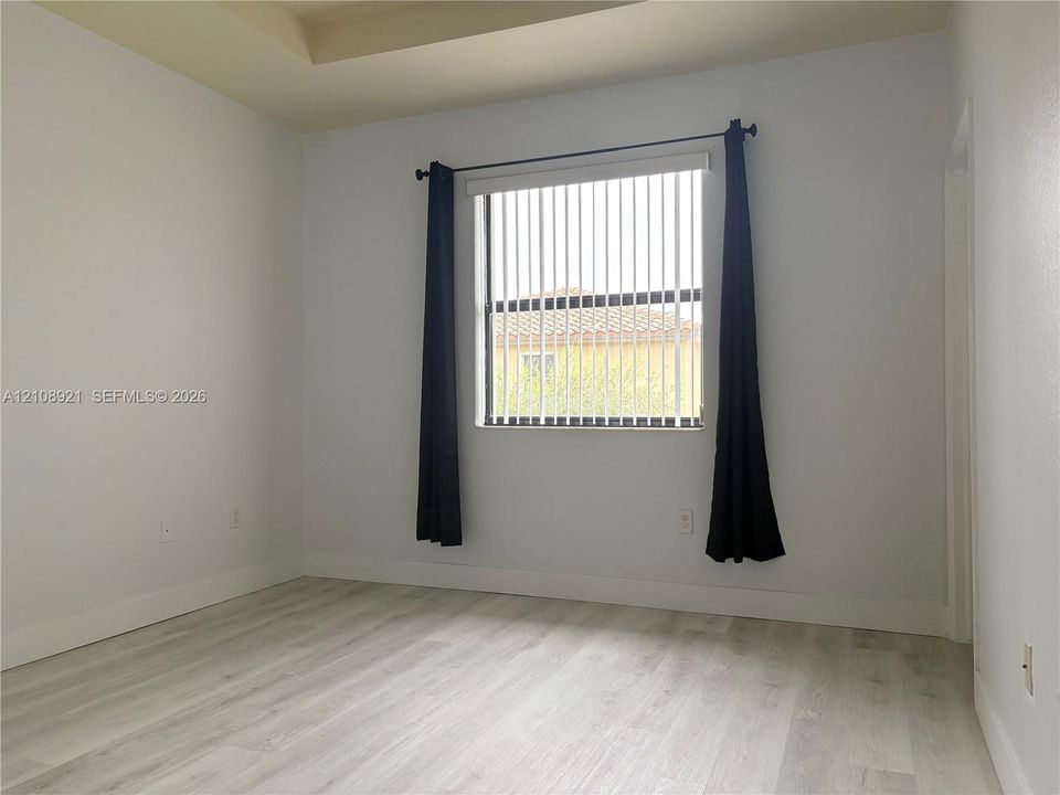 Interior room featuring tray ceiling, wood-finish flooring, and a single window with vertical blinds
