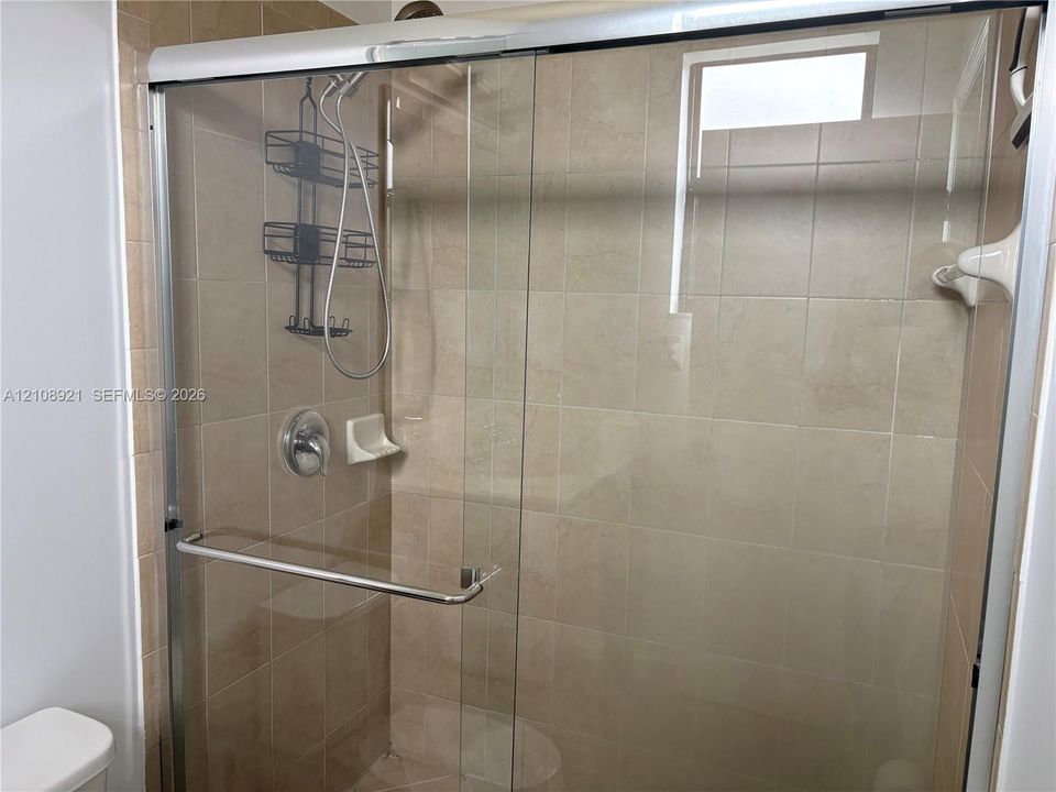 Walk-in shower enclosure featuring floor-to-ceiling neutral ceramic tiling, a sliding glass door with chrome hardware, and an integrated handheld shower fixture