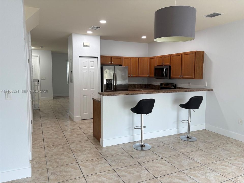 Kitchen featuring wood cabinetry, stainless steel refrigerator, built-in microwave, stone-finish breakfast bar, and tile flooring