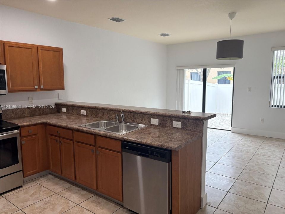 Kitchen featuring wood-finish cabinetry, stone-texture countertops, stainless steel dishwasher, double-basin sink, and ceramic tile flooring