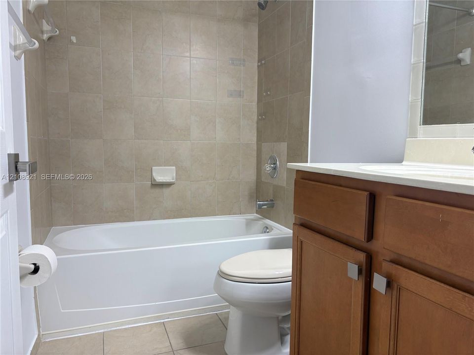 Bathroom featuring a tub-shower combination with floor-to-ceiling tile surround, wood-finish vanity cabinetry, countertop sink, and neutral ceramic tile flooring