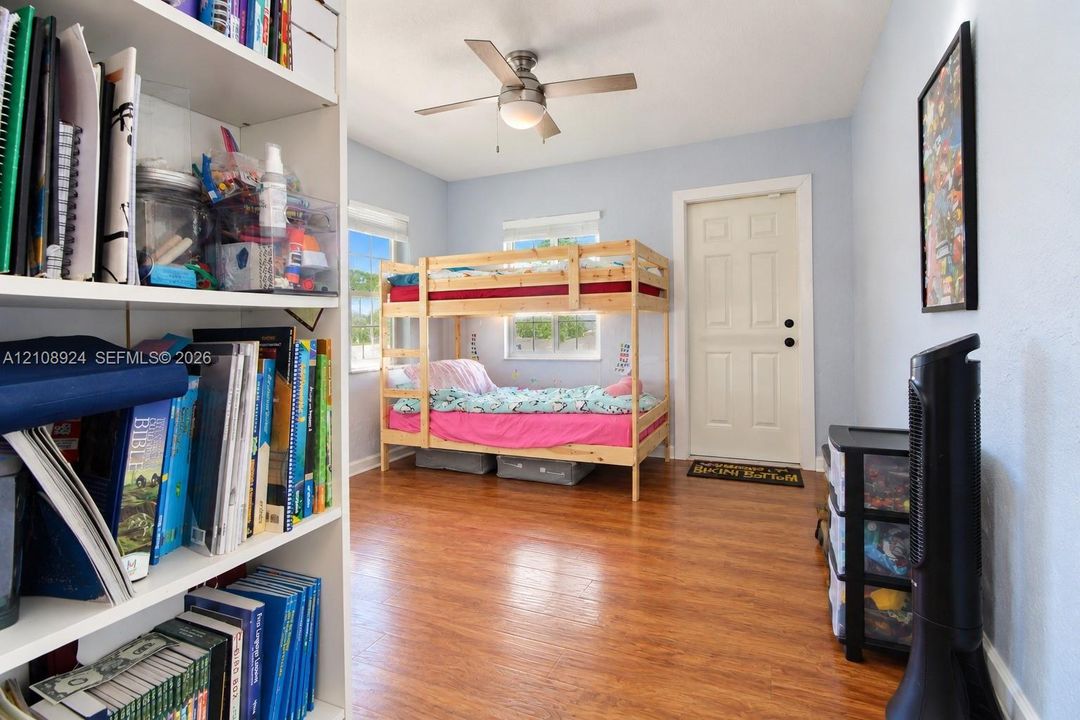 Room featuring wood-finish flooring, a centrally mounted ceiling fan with integrated light fixture, dual windows, and a six-panel interior door