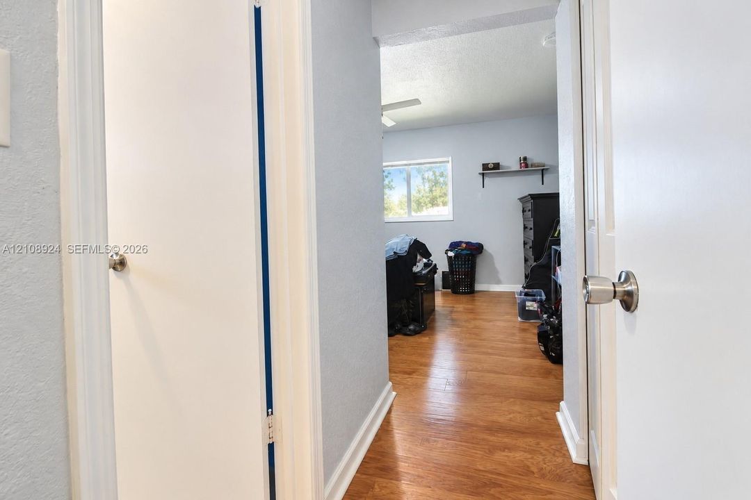 Hallway featuring wood-finish flooring, white paneled doors with metallic hardware, and light-toned wall paint