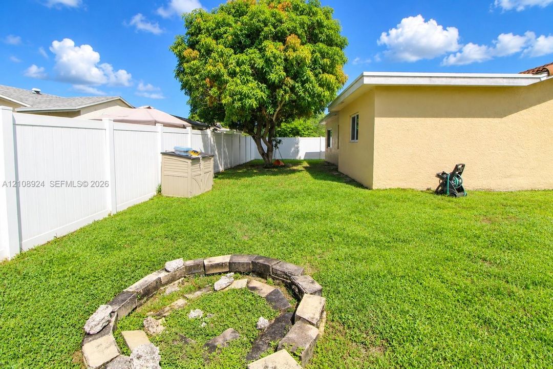 Private backyard featuring a grass lawn, perimeter vinyl fencing, and a stone-lined fire pit