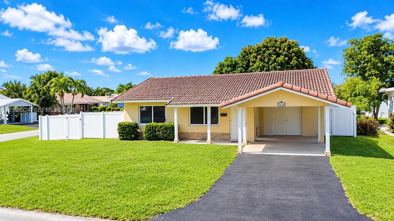 Single-story residence featuring a tile roof, covered carport, asphalt driveway, and white perimeter fencing