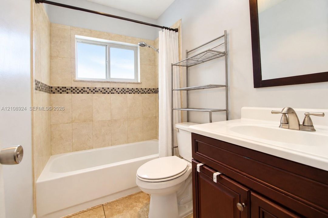 Bathroom featuring a vanity with a white countertop, tiled bathtub surround with a mosaic accent border, and tile flooring