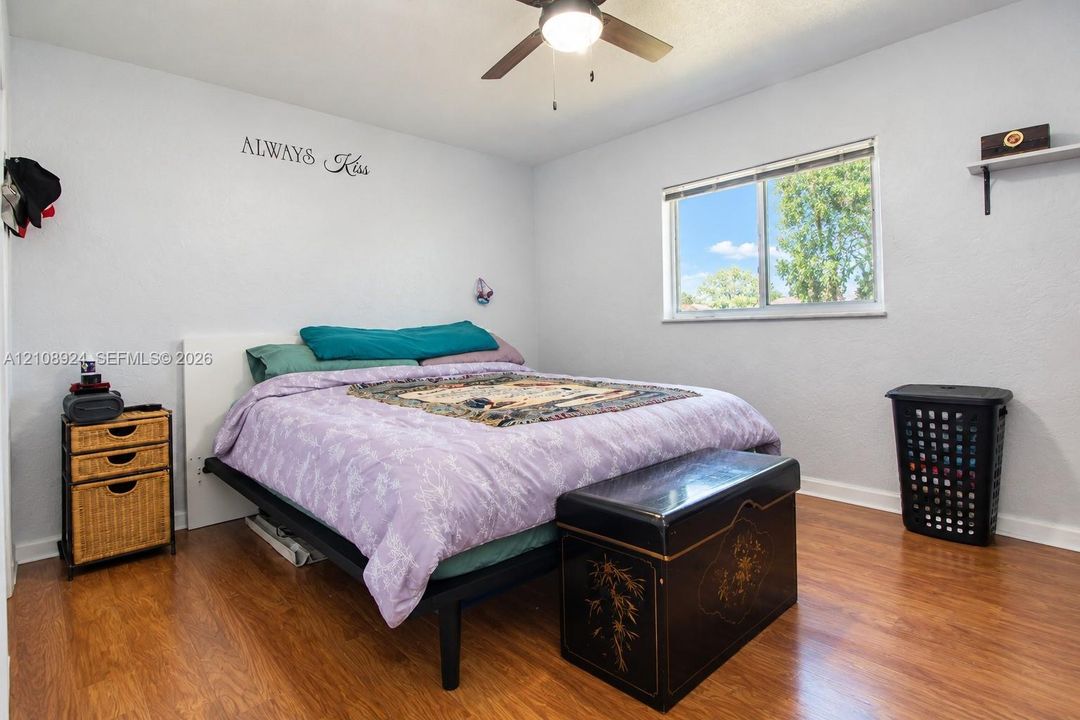 Bedroom featuring wood-finish flooring, a ceiling fan with integrated lighting, and a single-pane sliding window