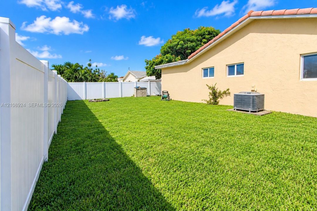 Private backyard featuring a manicured lawn, perimeter white vinyl fencing, and a stucco exterior finish